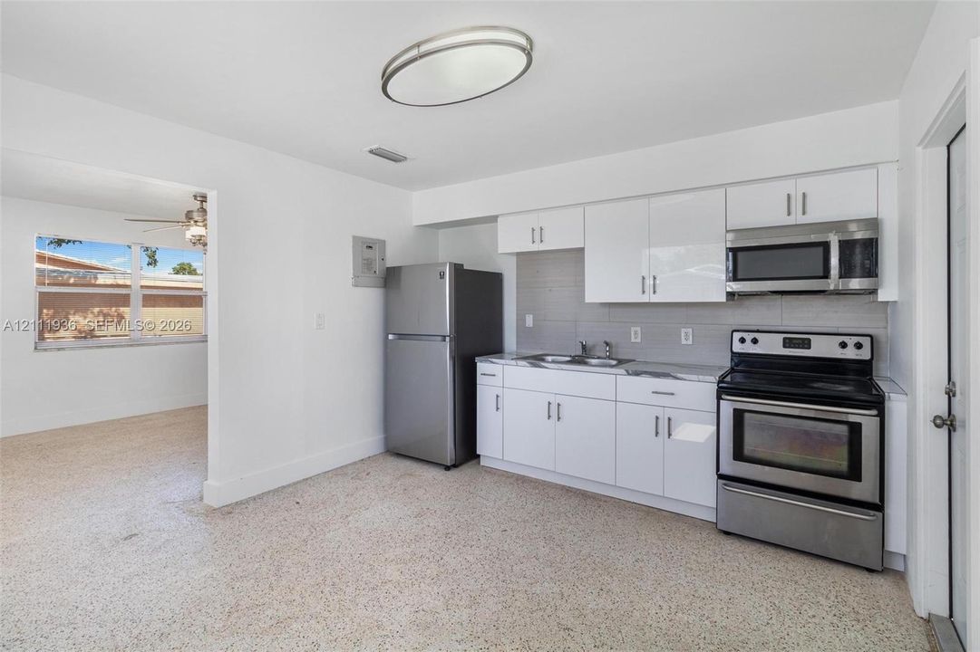 Kitchen featuring white high-gloss cabinetry, stainless steel appliances, stone-finish countertops, tiled backsplash, and light-toned composite flooring