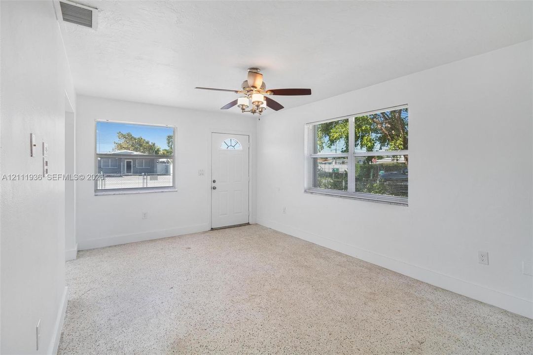 Neutral-toned interior featuring terrazzo flooring, white walls, dual-pane windows, and a multi-blade ceiling fan with integrated lighting