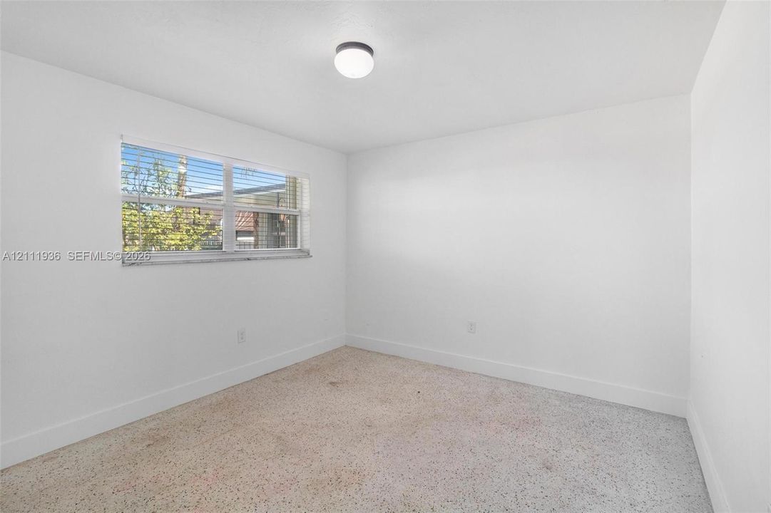 Bright room featuring white walls, a horizontal sliding window, and neutral terrazzo flooring with a flush-mount circular ceiling light