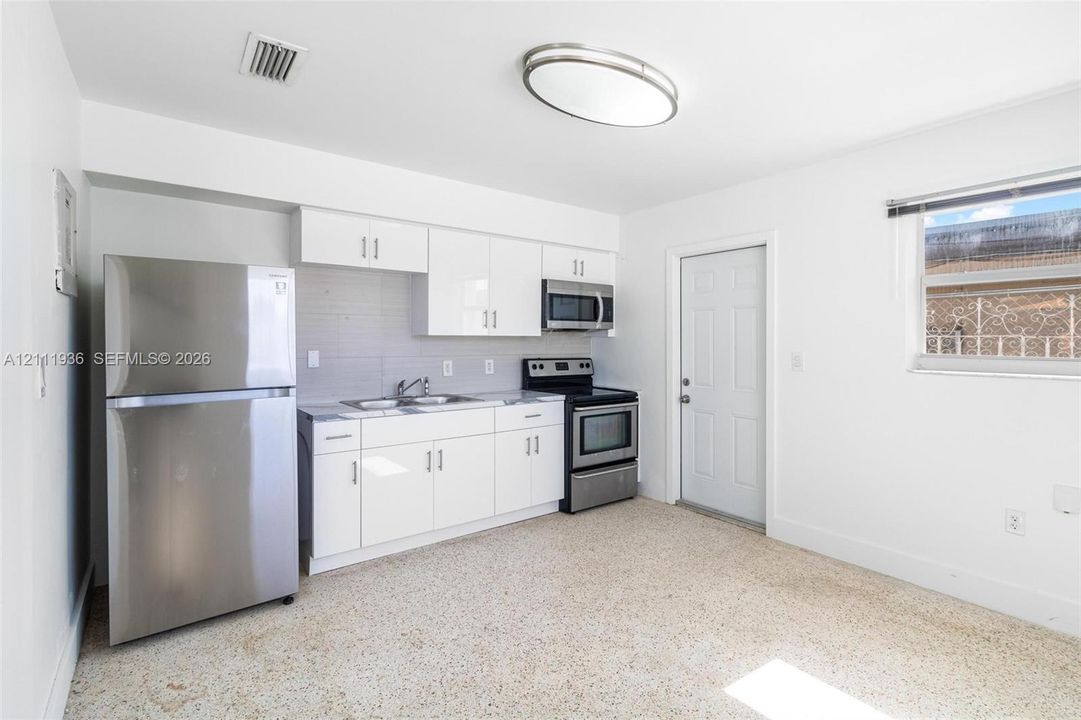 Kitchen featuring white shaker-style cabinetry, stainless steel appliances, a dual-basin sink, and terrazzo flooring