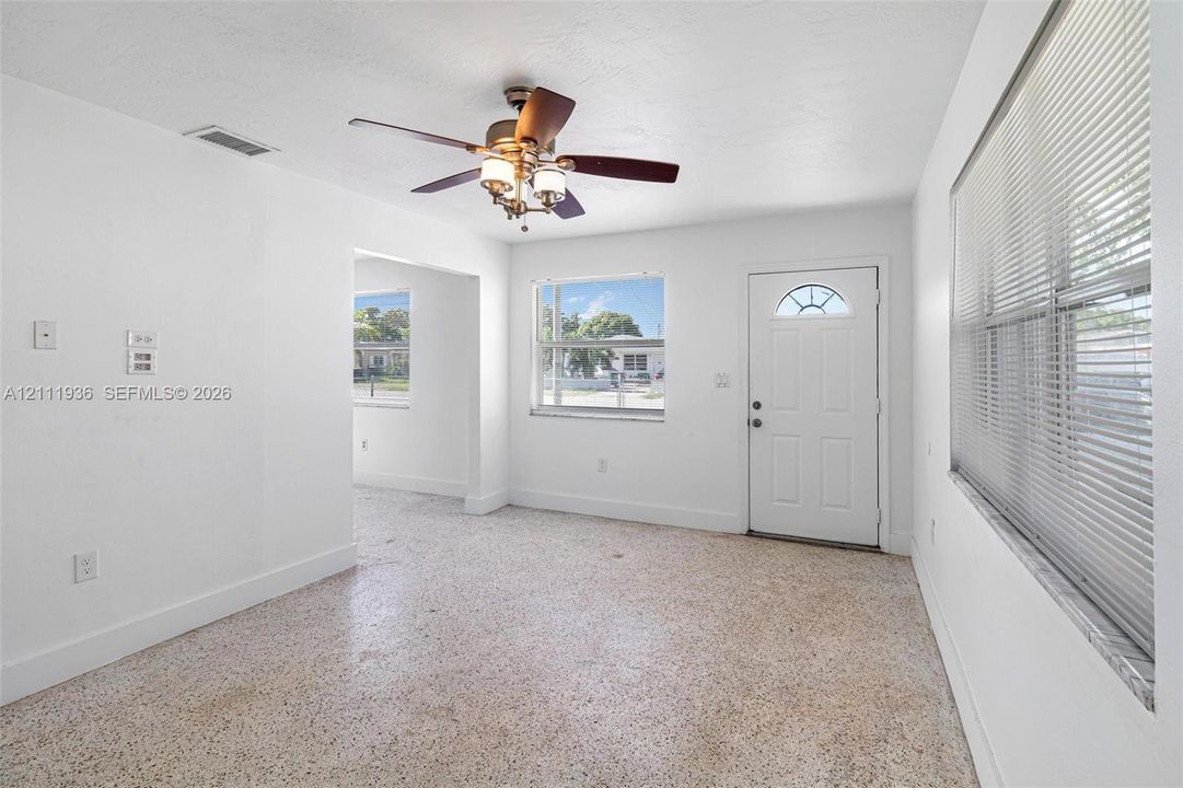 Interior space featuring terrazzo flooring, a ceiling fan with integrated lighting, a single-panel exterior door with a decorative arched window, and horizontal window blinds
