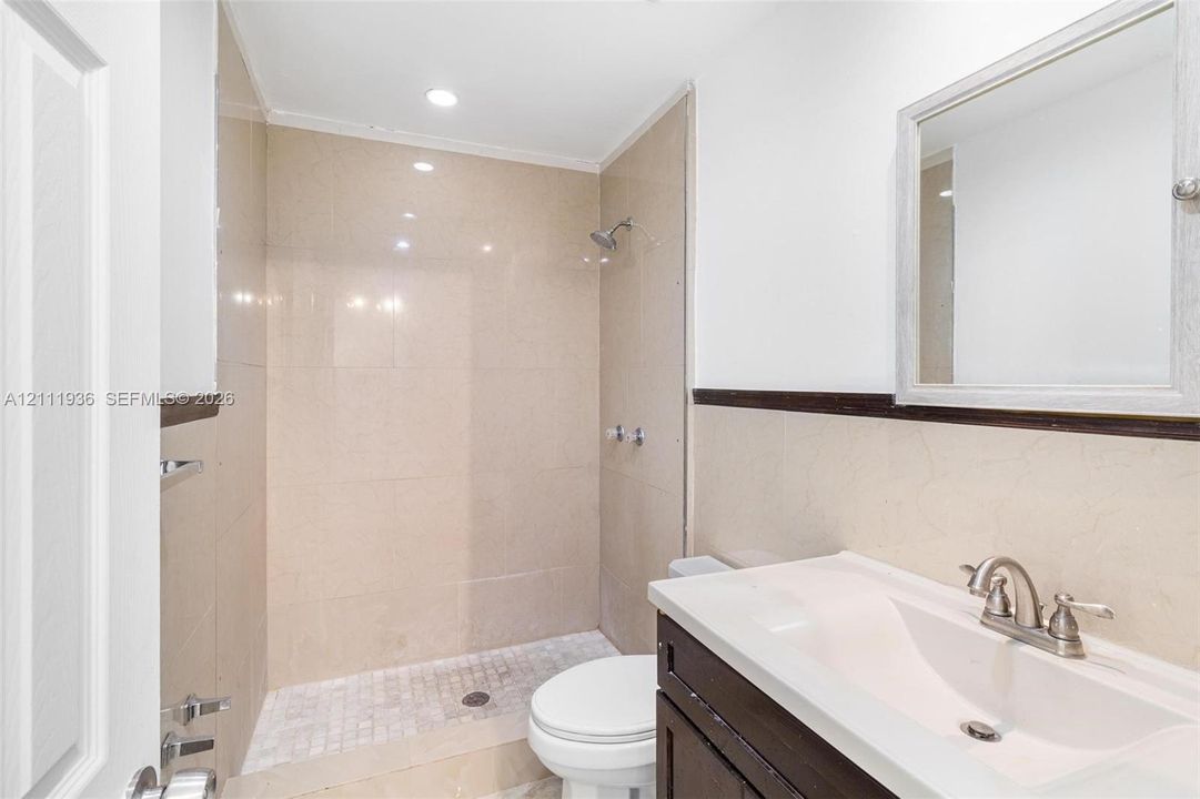 Bathroom featuring a walk-in shower with tiled surround, stone-mosaic shower floor, dark wood vanity, integrated sink, and recessed lighting
