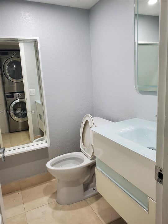 Bathroom featuring a wall-mounted floating vanity with an integrated sink, polished tile flooring, a tall beveled-edge mirror, and a built-in laundry area