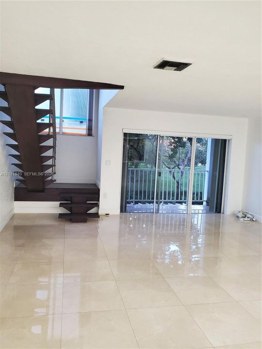 Open-concept interior featuring large-format tile flooring, a custom dark-toned floating staircase, and sliding glass doors leading to a private balcony