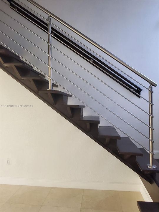 Staircase featuring dark-finish treads, a stainless steel horizontal cable railing system, and a mounted metal handrail