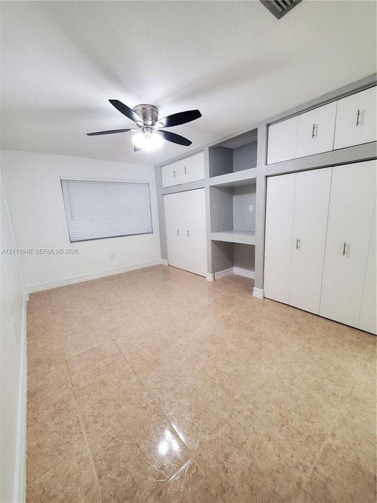 Tiled flooring and built-in wall cabinetry featuring white doors with silver-tone hardware, integrated shelving, and a central desk niche, complemented by a ceiling fan with integrated lighting