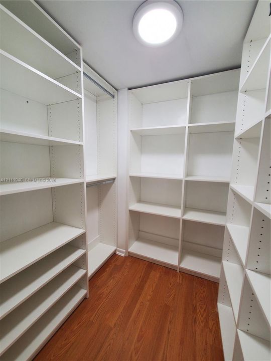 Custom walk-in storage featuring white built-in shelving, adjustable partitions, hanging rods, and wood-finish flooring
