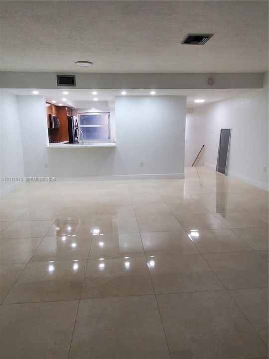 Polished large-format tile flooring, recessed ceiling lighting, and a breakfast bar pass-through opening to the kitchen