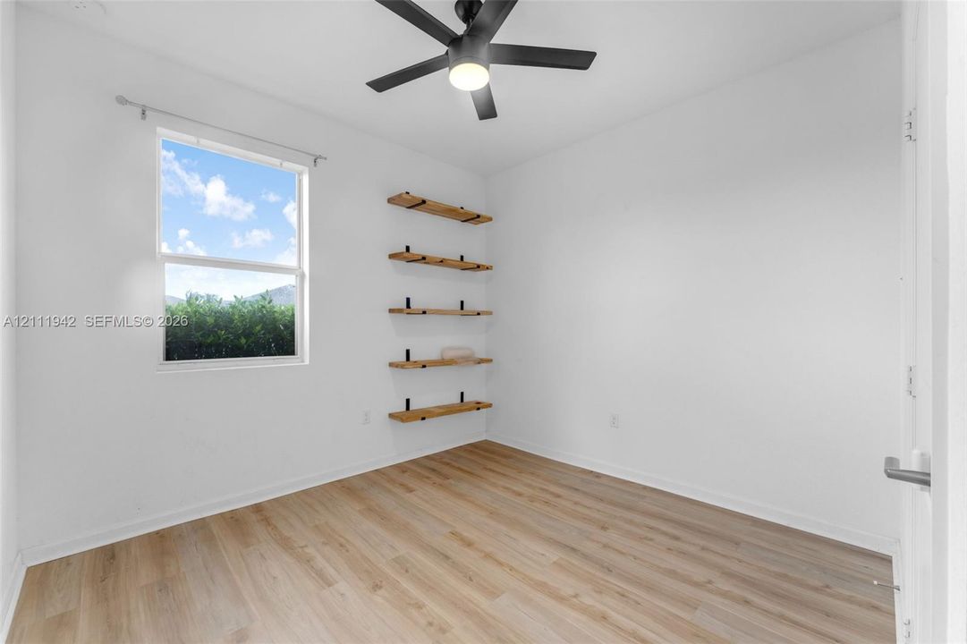 Wood-finish flooring, matte black ceiling fan, and wall-mounted natural wood shelving units