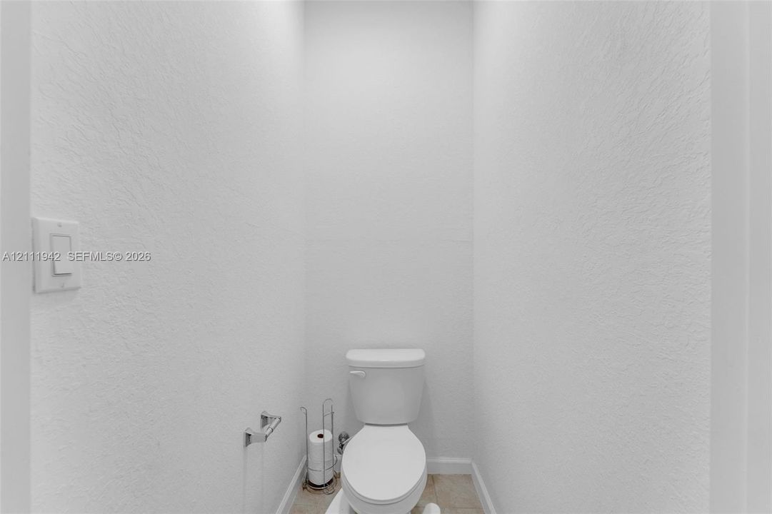 Restroom featuring neutral wall finishes, a white porcelain toilet, and a chrome-finish wall-mounted toilet paper holder