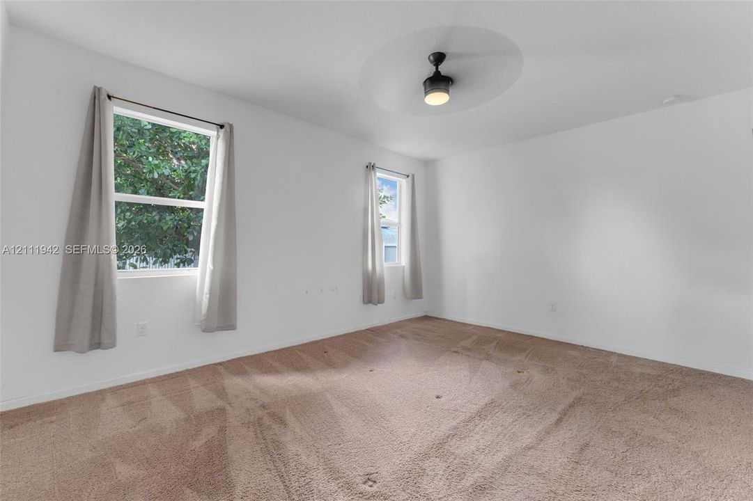 Neutral wall-to-wall carpeting, dual windows, and ceiling-mounted light fixture with integrated fan