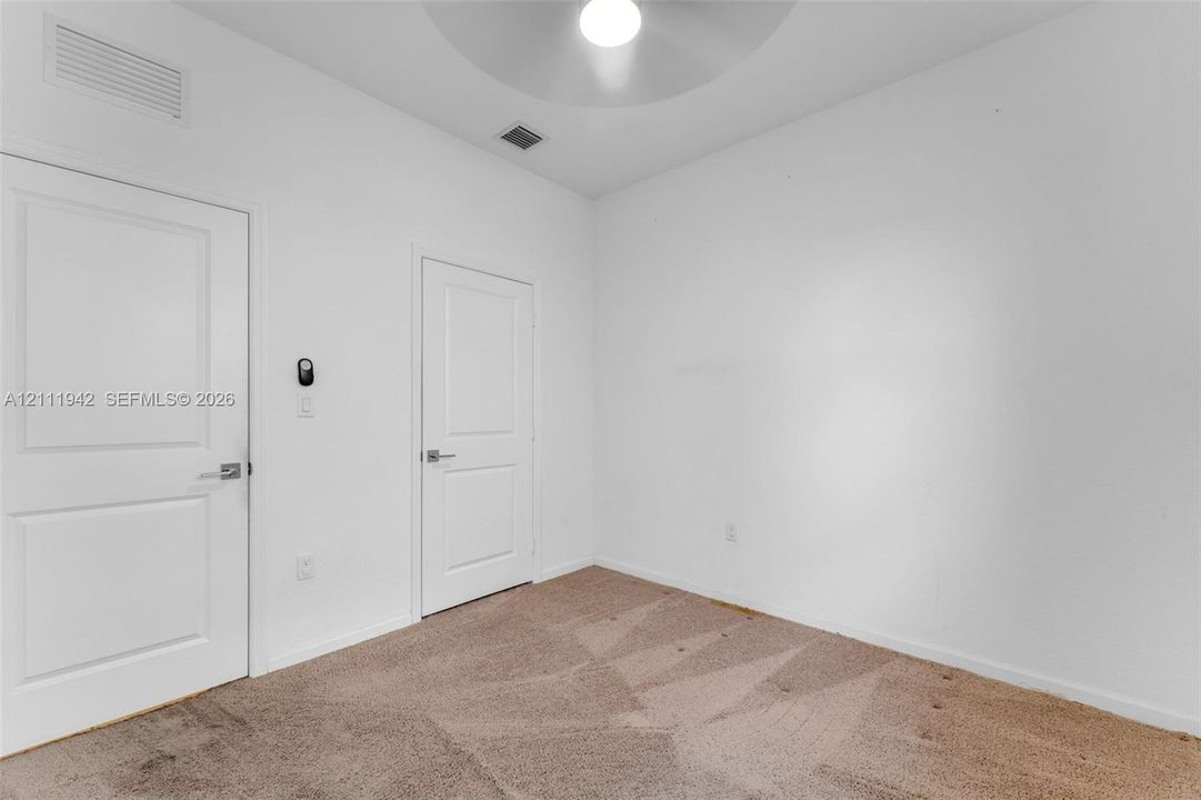 Neutral-toned carpeted flooring, two interior doors with panel detailing, and a central ceiling-mounted light fixture