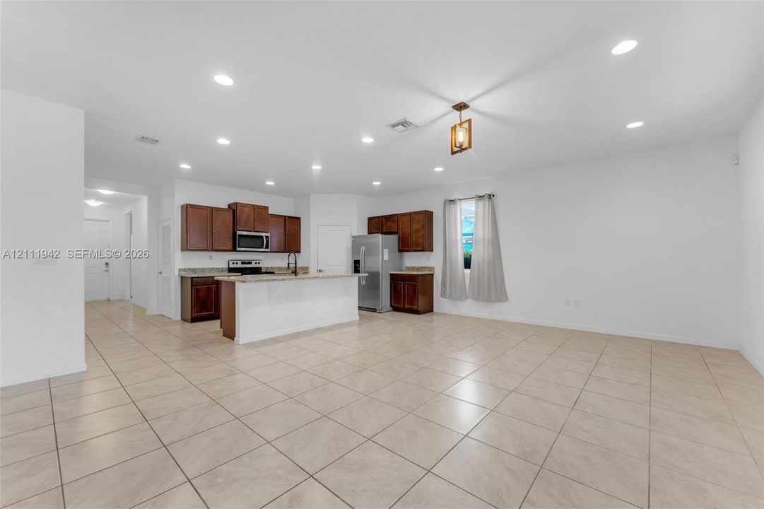 Open-concept interior featuring large-format tile flooring, recessed lighting, wood cabinetry, stone countertops, and a central kitchen island