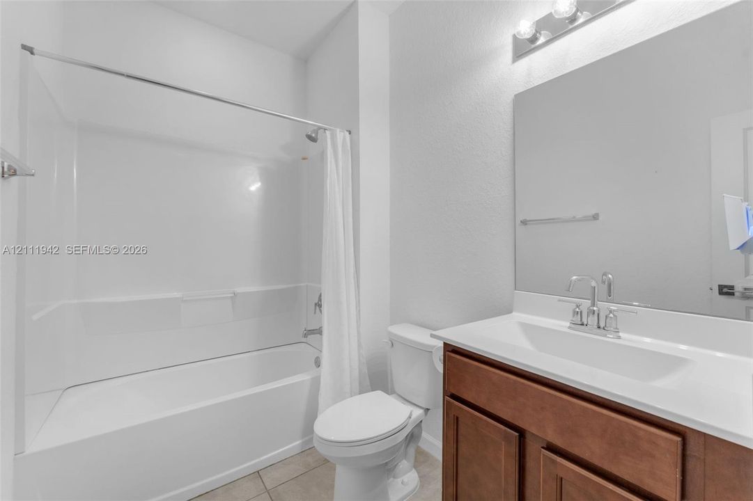 Bathroom featuring a white composite tub and shower surround, wood-finish vanity with an integrated countertop, large wall-mounted mirror, and overhead vanity lighting