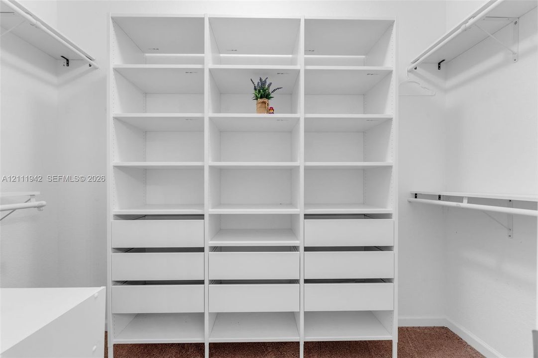 Walk-in closet featuring custom white shelving, integrated storage drawers, and overhead garment hanging rods