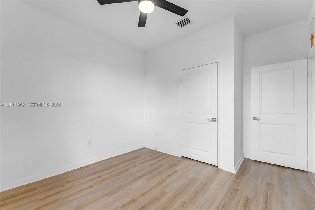 Room featuring wood-finish flooring, two white panel doors, and a ceiling-mounted light fixture with a fan