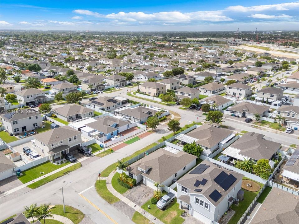 Aerial perspective of a suburban neighborhood featuring paved streets, multi-level residential structures, installed roof-mounted solar panels, and established landscaping