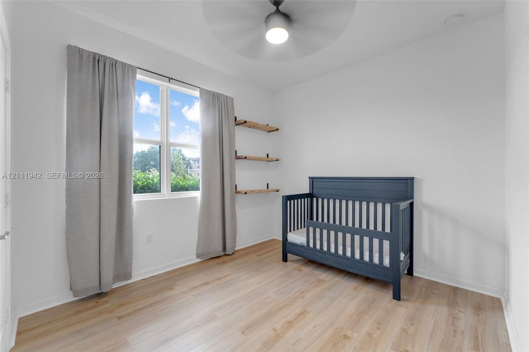Wood-finish flooring, multi-pane window, built-in wall shelving, and modern ceiling fan with integrated lighting