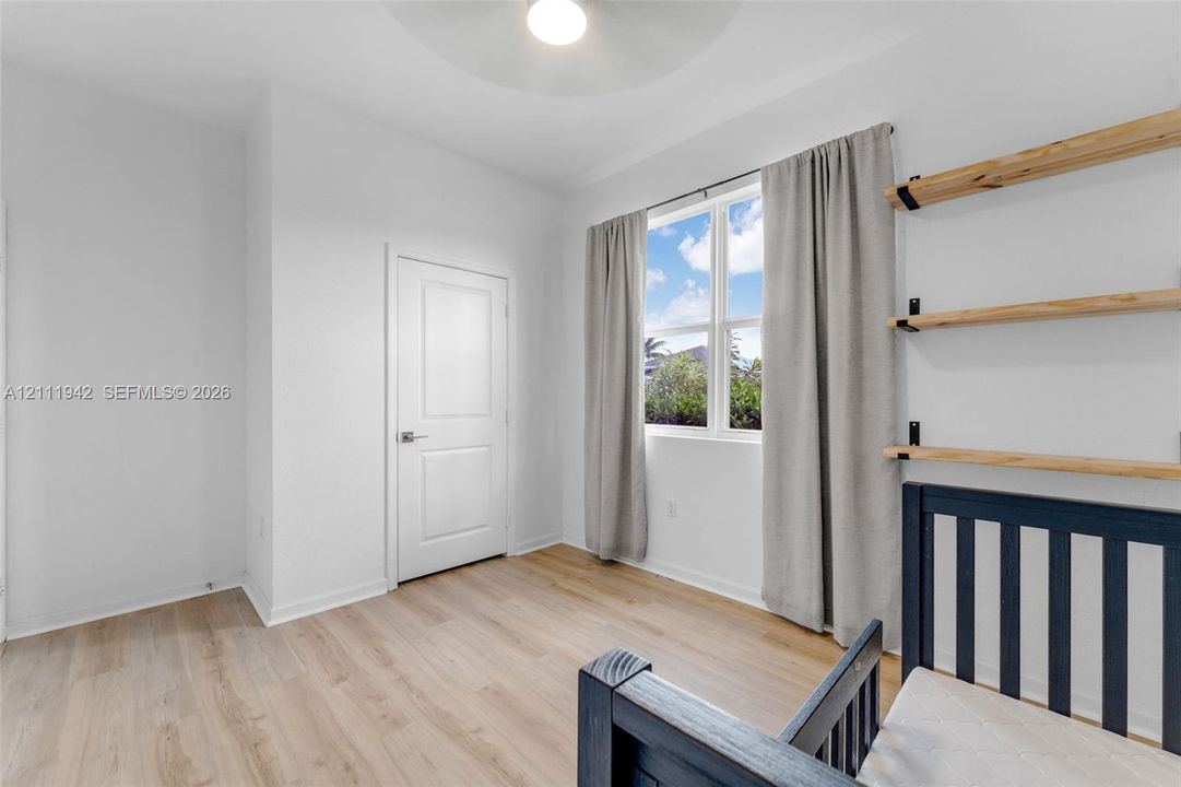 Room featuring light wood-finish flooring, a single-panel interior door, three wall-mounted natural wood shelves with metal brackets, and a ceiling-mounted light fixture