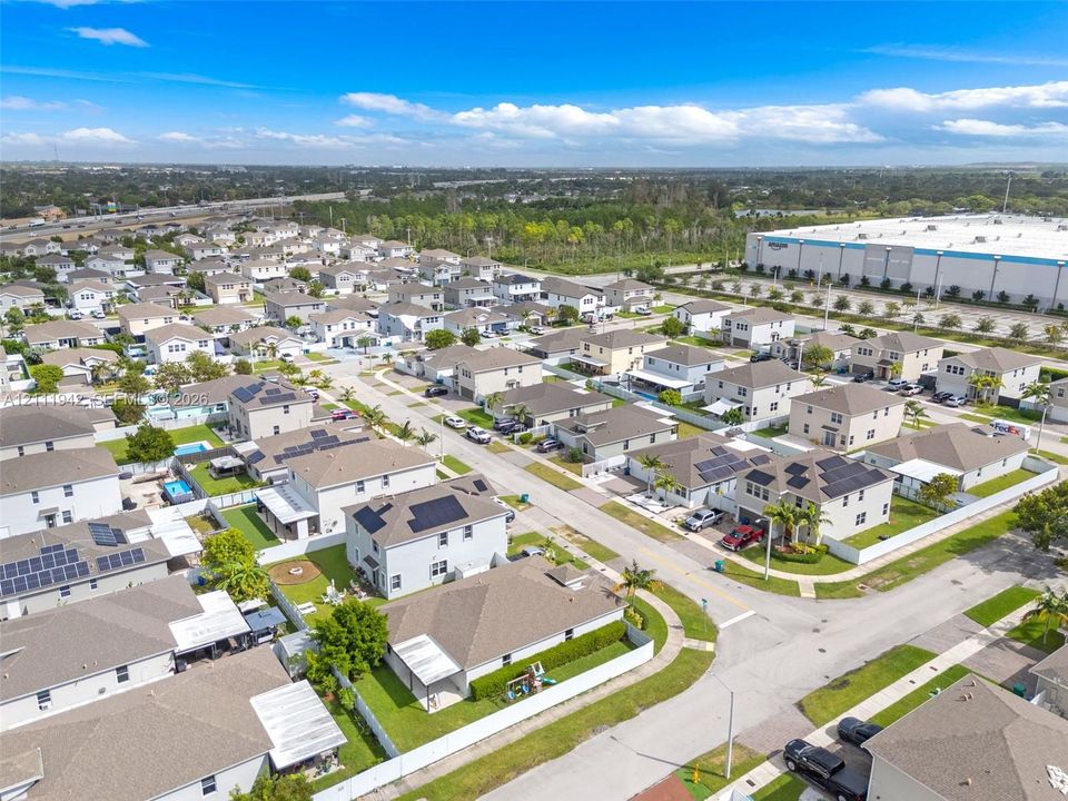Aerial perspective of a residential community featuring multi-story dwellings, shingle roofing, integrated solar panel systems, and private fenced yards