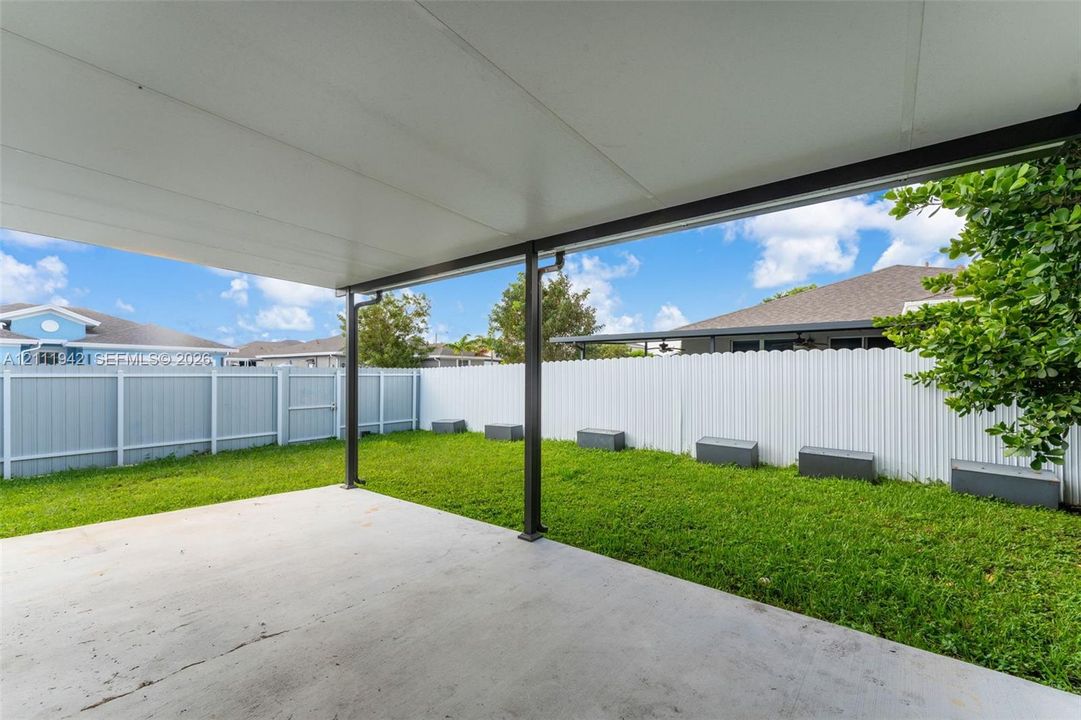 Covered concrete patio featuring a support column, enclosed by a white vinyl privacy fence with a lawn area