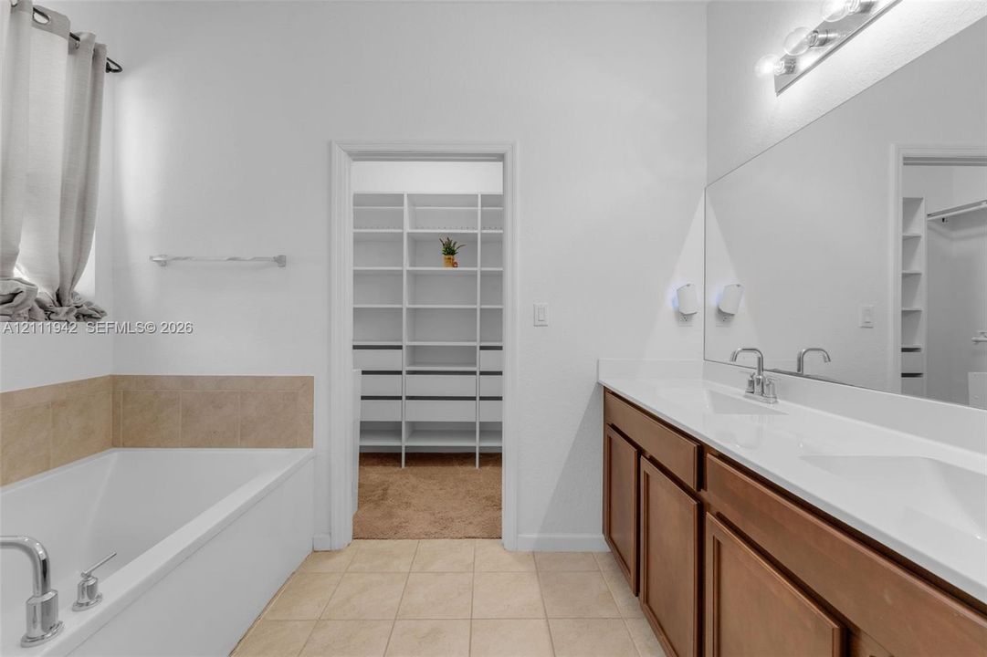 Double vanity with a white countertop and integrated dual sinks, soaking tub featuring tile surround, and a walk-in closet with built-in shelving