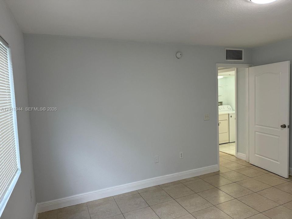Neutral-toned tile flooring, light-colored walls, horizontal window blinds, and a multi-panel interior door