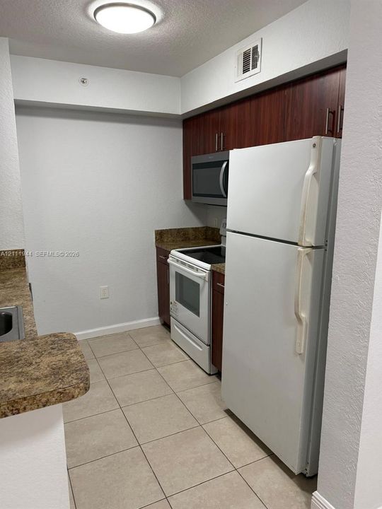 Kitchen featuring dark wood-finish cabinetry, stone-finish countertops, ceramic tile flooring, and white kitchen appliances including a built-in microwave