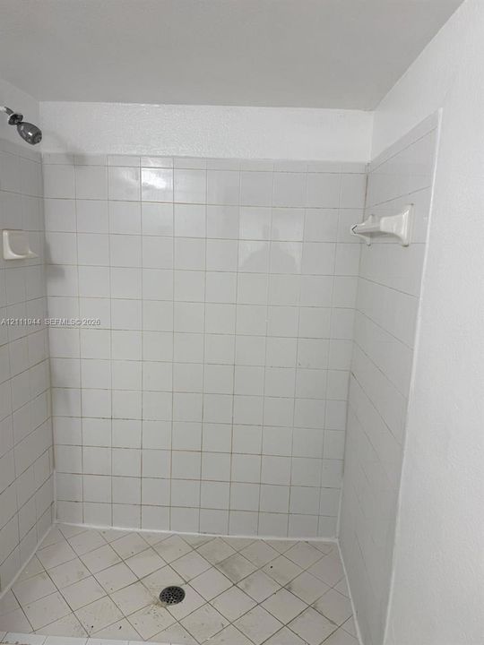 Shower enclosure featuring white square tile wall surround, built-in recessed soap dish, wall-mounted showerhead, and a built-in towel rack