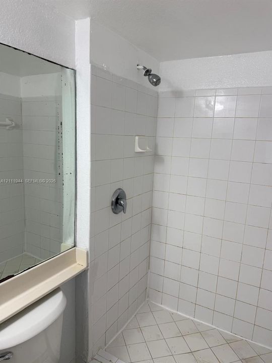 Shower enclosure featuring white square wall tile, a built-in recessed soap dish, chrome shower head and handle, and a flat-panel mirror