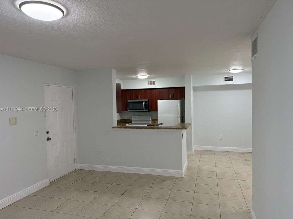 Open floor plan with large-format tile flooring, kitchen featuring dark wood cabinetry, breakfast bar, and integrated appliances