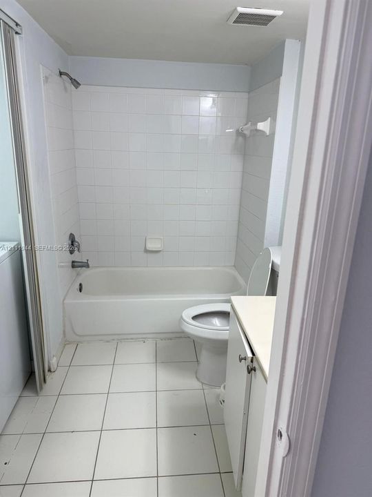 Bathroom featuring square tile flooring, a tub-shower combination with white ceramic wall tiling, a vanity with a solid-surface countertop, and a built-in recessed soap dish