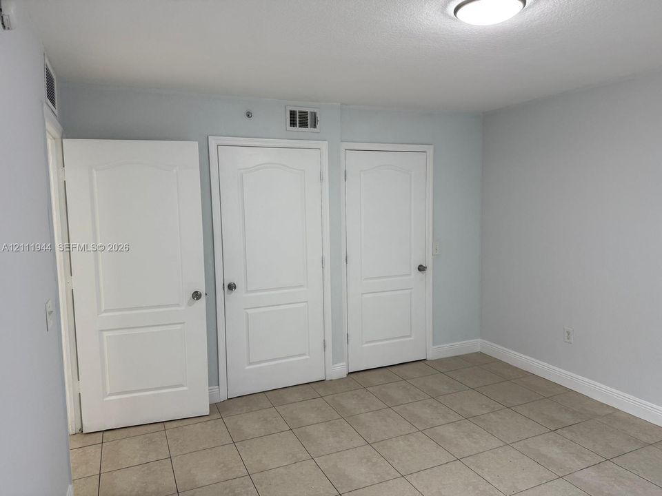 Neutral-toned interior space featuring ceramic tile flooring, three white two-panel interior doors, and a flush-mount ceiling light fixture