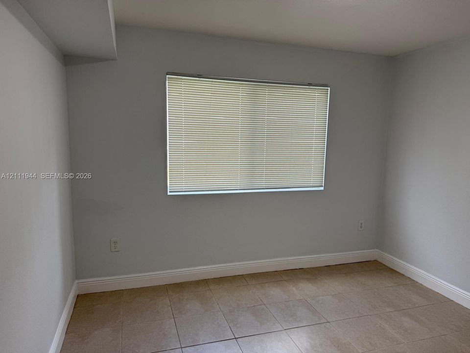 Neutral-toned interior space featuring light-colored tile flooring and a window with horizontal blinds