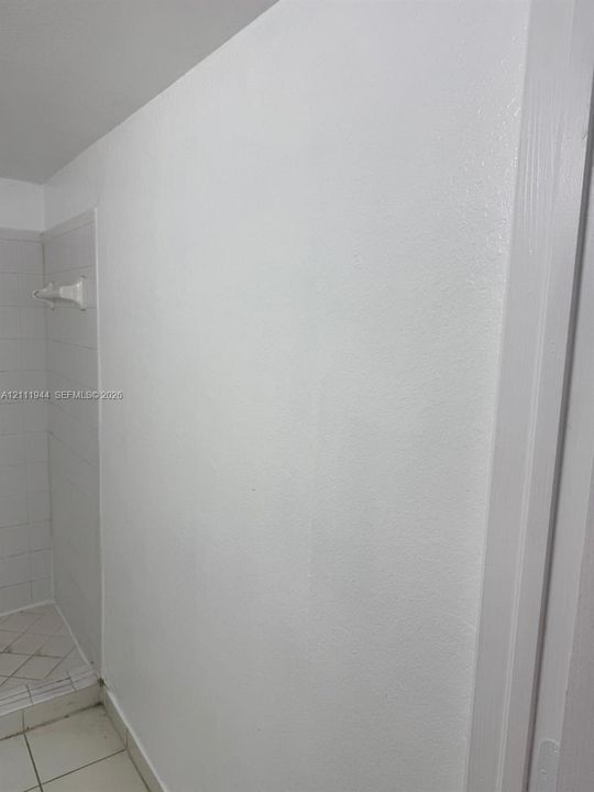 Neutral interior wall featuring white paint finish with a tiled shower enclosure, white wall-mounted towel bar, and square floor tiles