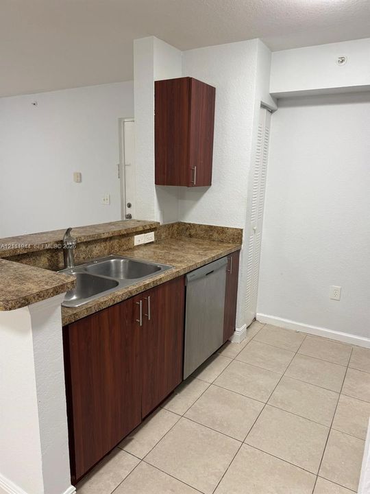 Kitchen featuring dark wood-finish cabinetry, stone-pattern laminate countertops, stainless steel dual-basin sink, integrated dishwasher, and tile flooring