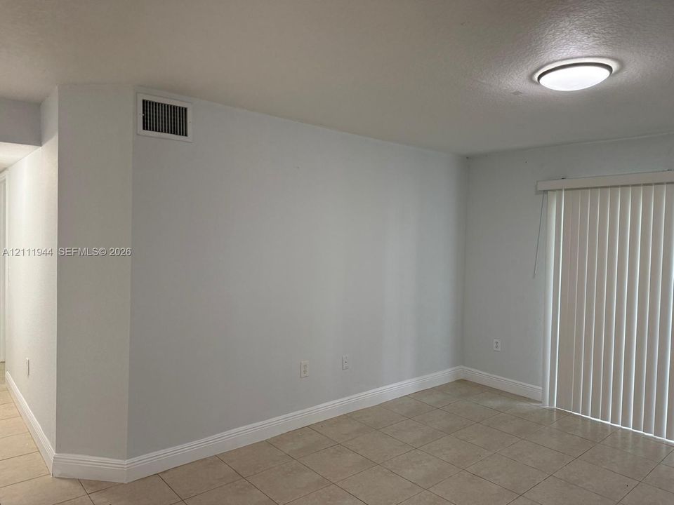 Interior space featuring neutral wall paint, tile flooring, and sliding glass door with vertical blinds