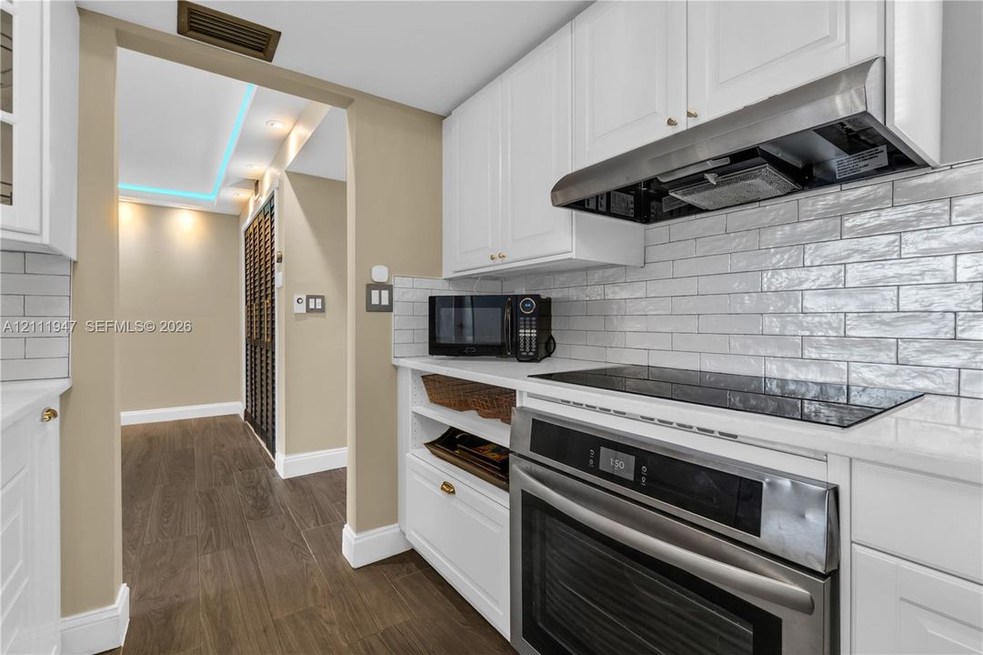 Kitchen featuring white shaker-style cabinetry, a glossy subway tile backsplash, stone countertops, integrated stainless steel appliances, and wood-finish flooring