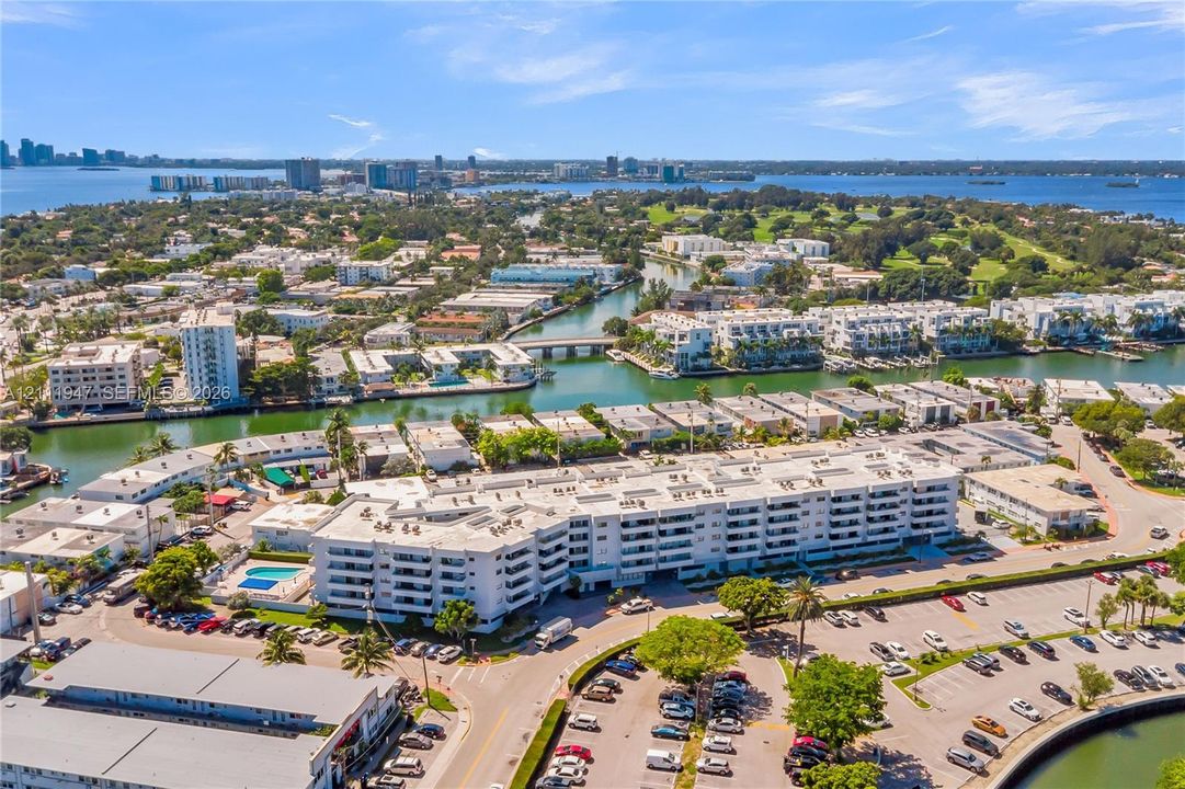 Aerial perspective of a multi-story residential building featuring private balconies, a communal pool, landscaped grounds, and proximity to waterfront canals