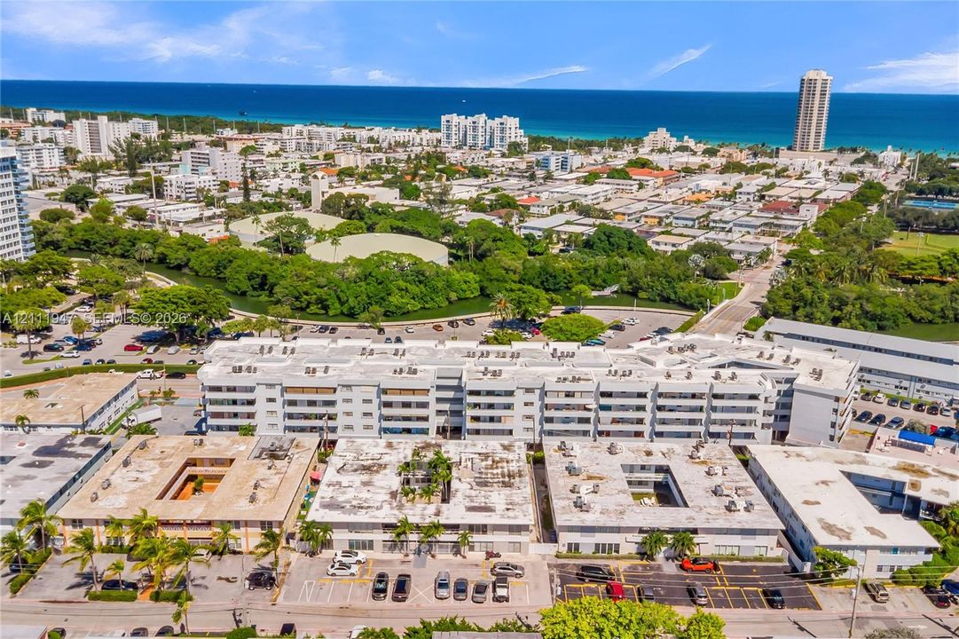 Aerial perspective of a multi-story residential building featuring exterior balconies, on-site surface parking, and coastal surroundings