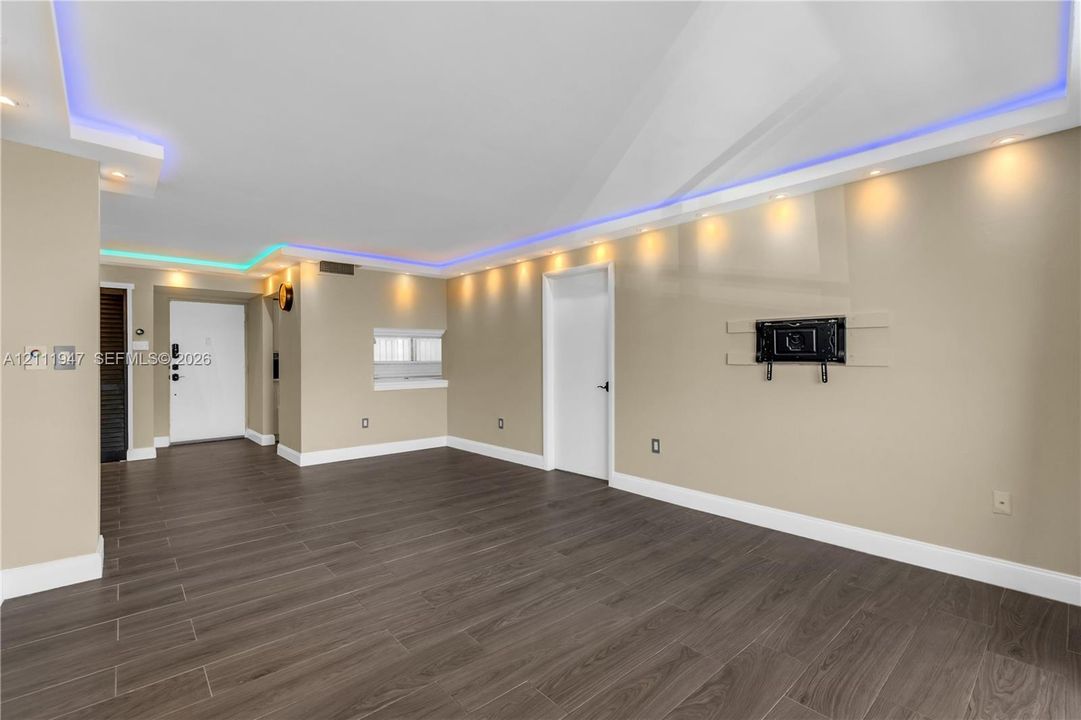 Wood-finish flooring, recessed lighting, integrated perimeter accent lighting, and a wall-mounted media bracket