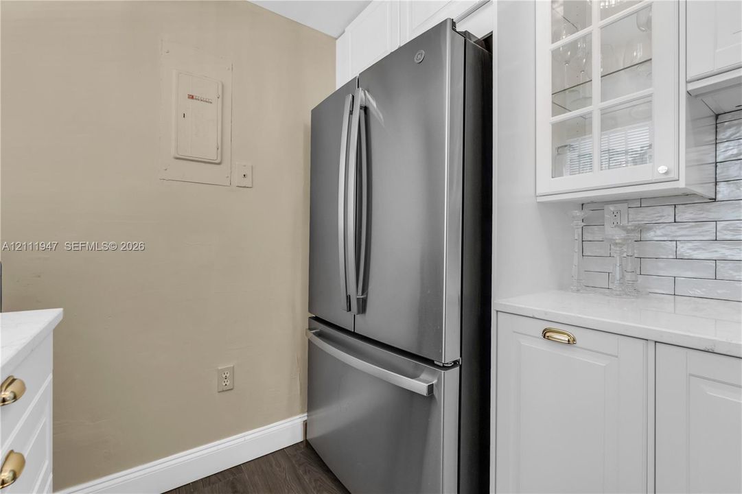 Stainless steel French-door refrigerator, white shaker-style cabinetry, glass-front upper cabinet, stone-surface countertop, and horizontal subway tile backsplash