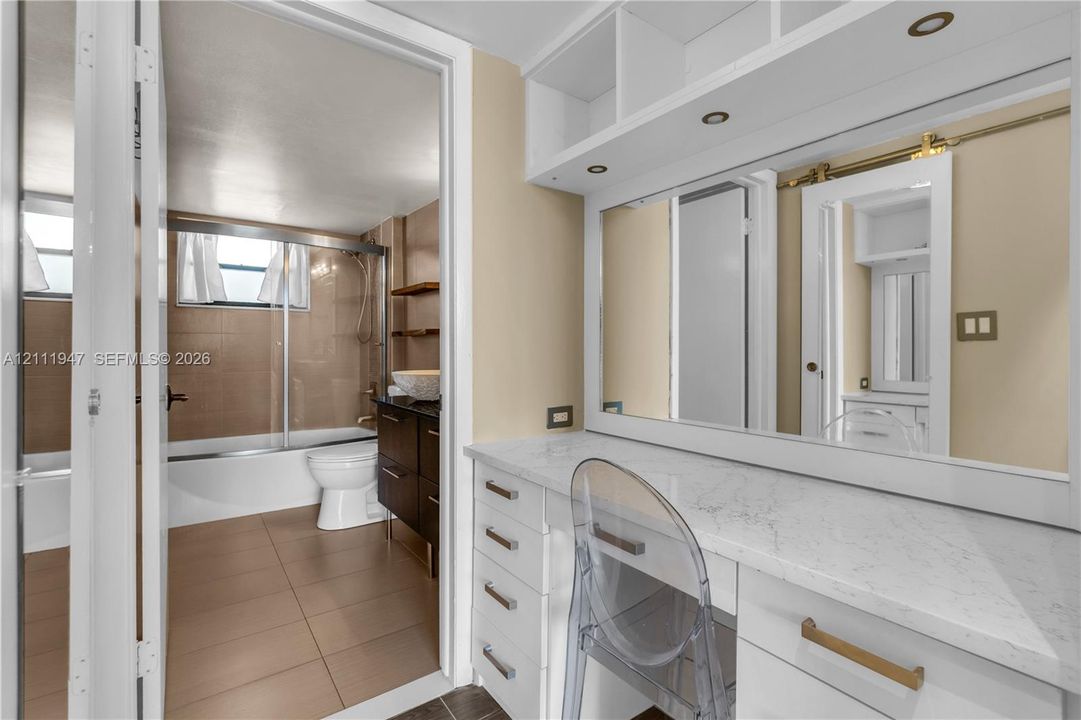 Built-in white vanity with stone-finish countertop, full-width mirror, overhead cabinet storage, and integrated recessed lighting