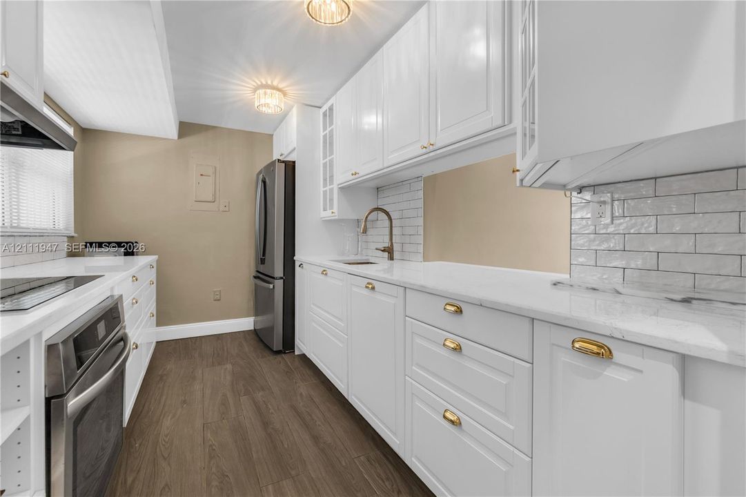 Kitchen featuring white shaker cabinetry, stone-finish countertops, subway tile backsplash, stainless steel appliances, and wood-finish flooring