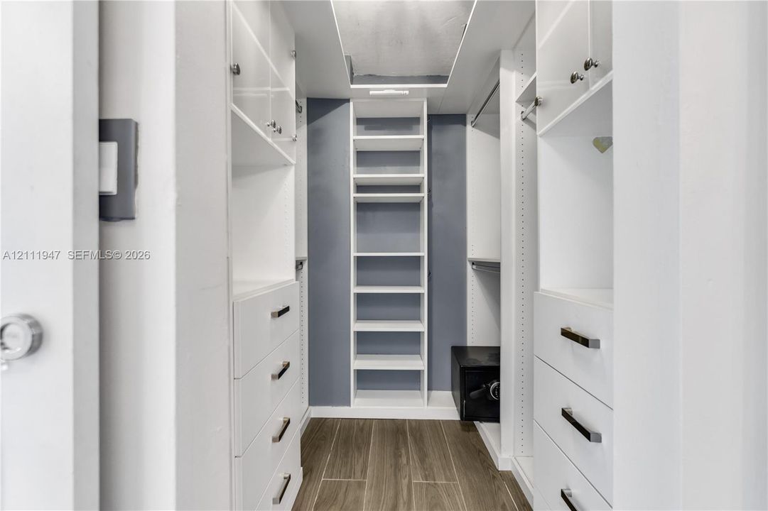 Walk-in closet featuring white cabinetry, built-in shelving, integrated drawers with metallic pulls, and wood-finish flooring