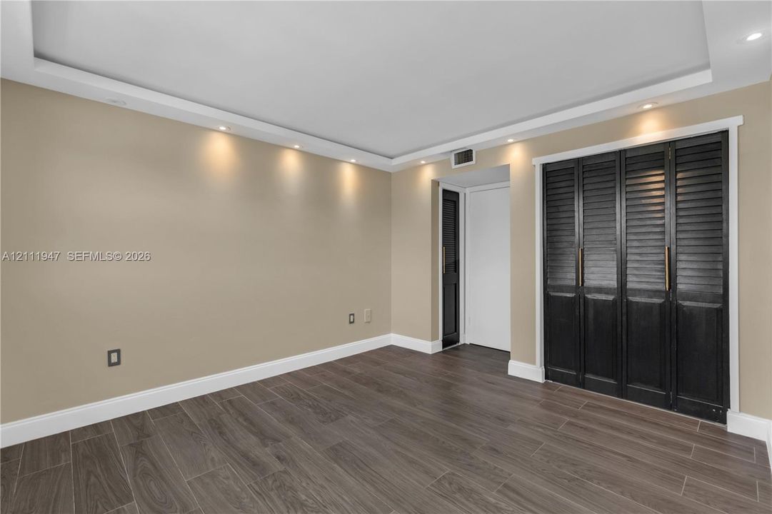 Room featuring recessed tray ceiling lighting, wood-finish tile flooring, and floor-to-ceiling bi-fold closet doors with metallic pulls