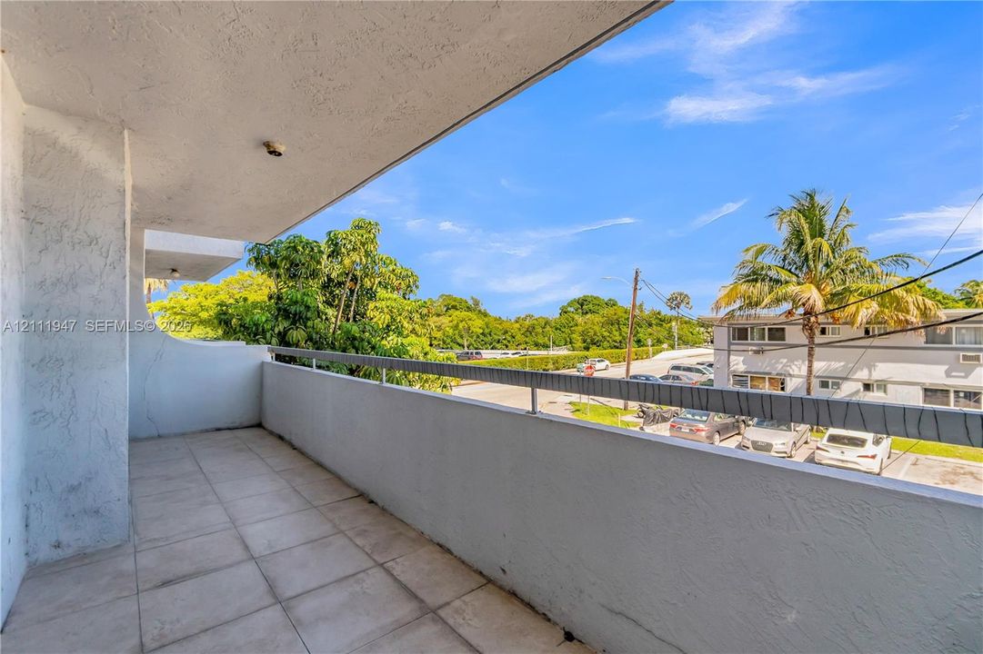 Covered balcony featuring tile flooring, smooth stucco wall finishes, and a metal railing