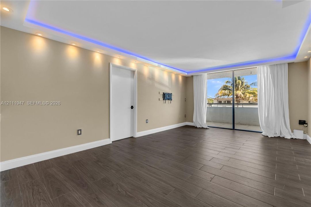 Interior space featuring wood-finish flooring, recessed ceiling lighting, integrated blue LED perimeter accent lighting, and a large sliding glass door opening to a private balcony