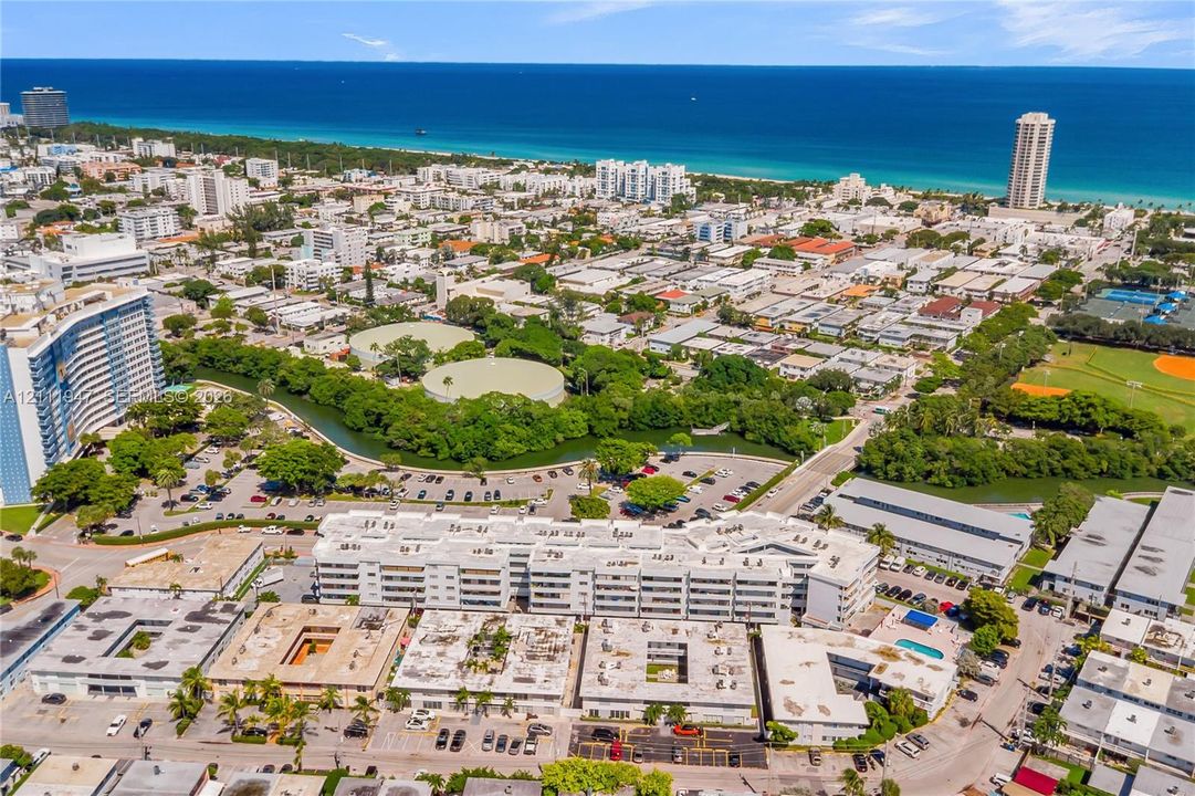 Aerial perspective showcasing a multi-story residential complex featuring paved parking areas, a centralized courtyard, and an outdoor swimming pool
