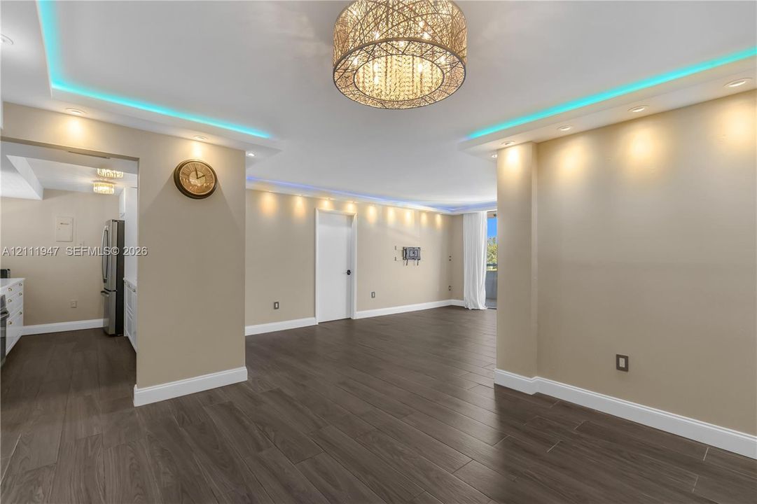 Open-concept space featuring wood-finish flooring, recessed lighting, crown molding with integrated accent lighting, and a drum-style chandelier with crystal detailing